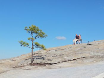 People standing on rock against blue sky