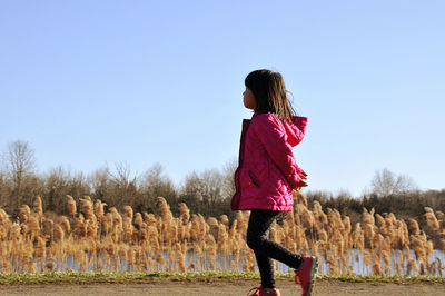 Side view of girl walking on field against clear sky