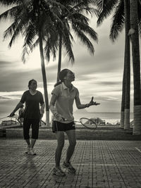 People standing on palm tree by sea against sky