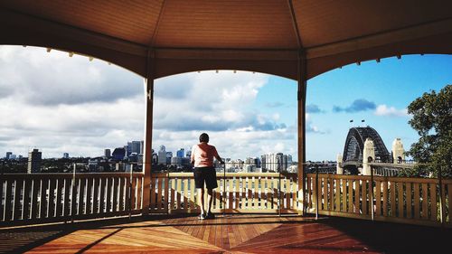 Rear view of man standing in gazebo against city