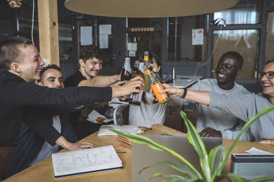 Smiling colleagues toasting beer at workplace