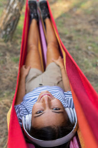 Peaceful female in headphones lying in hammock and enjoying calm music and looking at camera