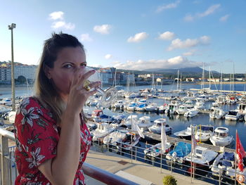 Portrait of young woman drinking wine against harbor