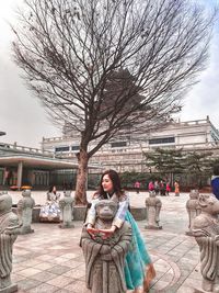 Women sitting on tree in city against sky