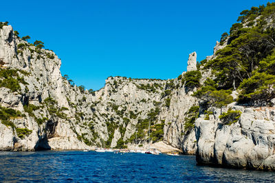 Low angle view of cliff by sea against clear blue sky