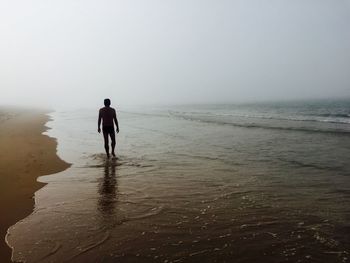 Man wading in sea against sky
