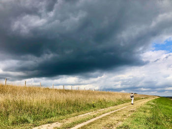 Rear view of man on road amidst field against sky