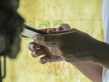 Close-up of man holding smart phone against yellow fabric