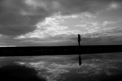 Silhouette man standing by swimming pool against sky
