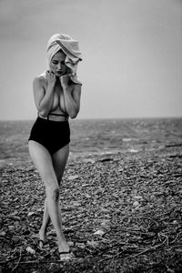 Full length of young woman standing on beach against sky