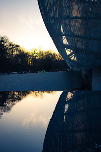 Reflection of trees in swimming pool against lake during sunset