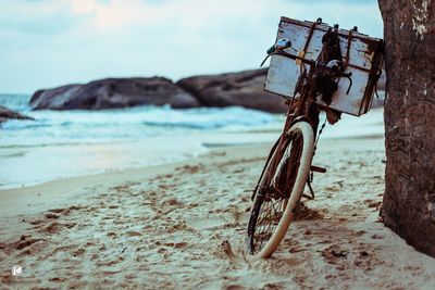 Old bicycle at beach against sky