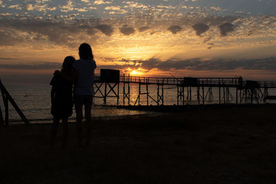 Rear view of silhouette girls on beach against sky during sunset