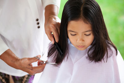 Midsection of grandmother cutting granddaughter hair