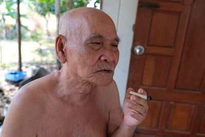 Shirtless senior man smoking cigarette while sitting outdoors