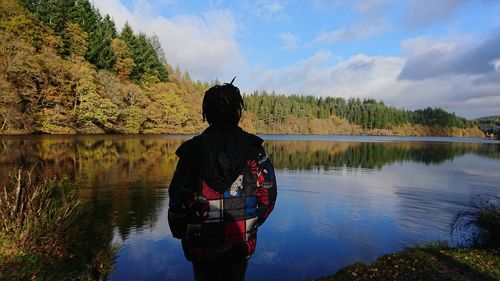 Rear view of boy wearing jacket while standing by lake against sky