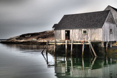 Wooden house by lake against sky