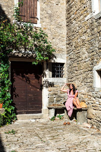 Beautiful young woman sitting on stone bench, rustic house, vintage, picturesque, town, travel.