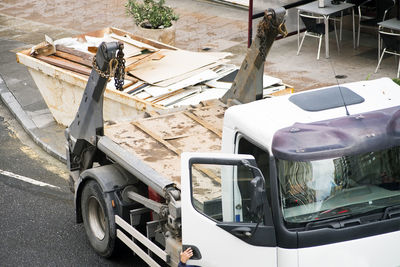 Construction worker with metal container in truck with debris and wood waste