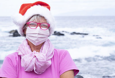 Portrait of senior woman wearing mask standing against sea