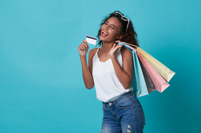 Portrait of happy woman holding shopping bags while standing against turquoise background