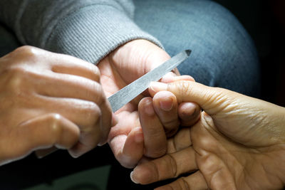 Cropped hands of woman filing customer fingernails at spa