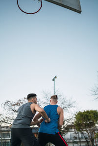 Young men playing basketball against sky