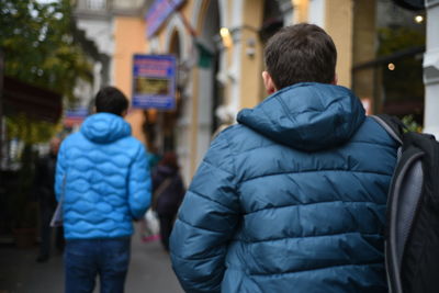 Rear view of man in hooded jacket while walking on footpath