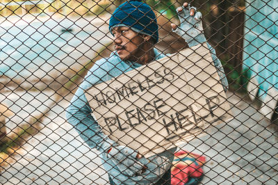 Full length portrait of woman standing by chainlink fence