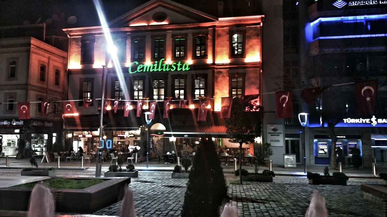 architecture, built structure, building exterior, illuminated, night, chair, city, restaurant, incidental people, window, street, lighting equipment, empty, entrance, absence, architectural column, table, building, sidewalk, outdoors