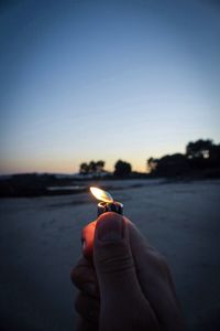 Close-up of person holding cigarette lighter against sky at sunset