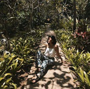 Full length of woman sitting on footpath amidst trees