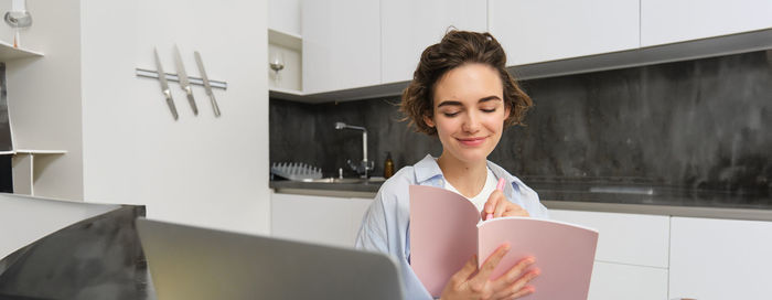 Portrait of young woman using mobile phone while standing in office