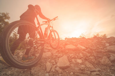 Man carrying bicycle on field against orange sky