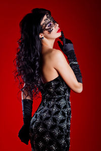 Fashion model wearing mask standing against red background