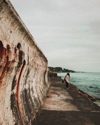 Woman standing on wall by sea against sky