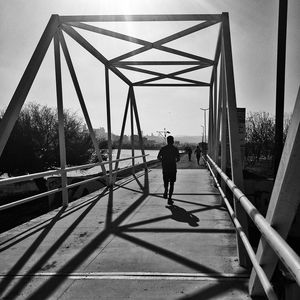 Rear view of man walking on bridge against sky