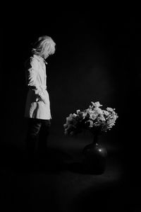 Midsection of woman standing by flower vase against black background