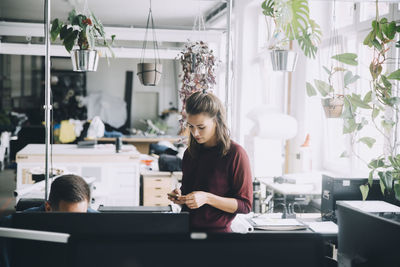 Businesswoman using mobile phone while standing by male colleague in creative office