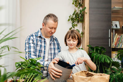 A teenage girl helps her dad to transplant a monstera houseplant into another pot. 