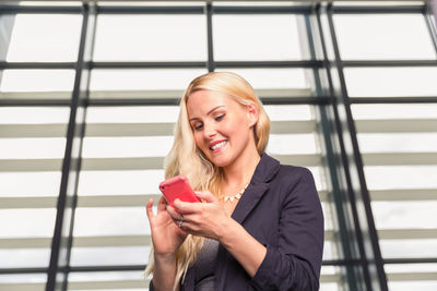 Happy woman using smartphone near wall