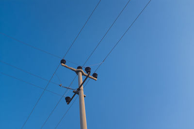 Low angle view of birds on cable against clear blue sky