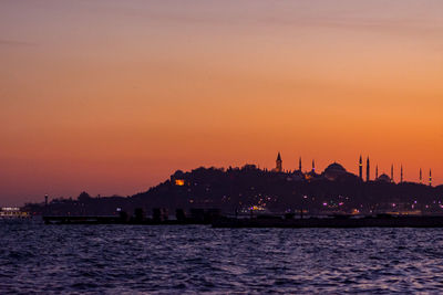 Silhouette buildings by sea against sky during sunset