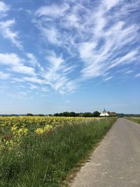 Road passing through field against cloudy sky