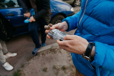 Midsection of man holding blue while sitting on car