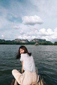 Smiling woman sitting on wooden raft over lake against sky