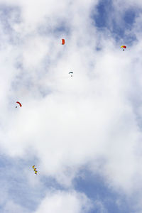 Low angle view of people paragliding against cloudy sky