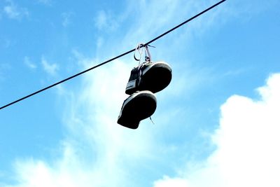 Low angle view of shoes hanging on cable against blue sky