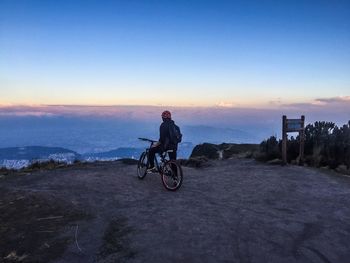 Man riding bicycle on mountain peak against sky during sunset