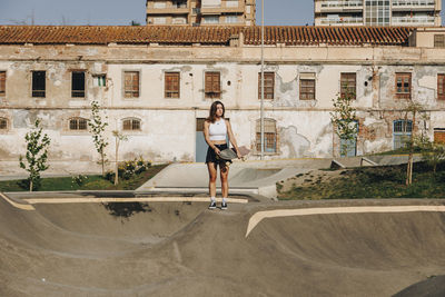 Young woman with skateboard at skate park in front of building